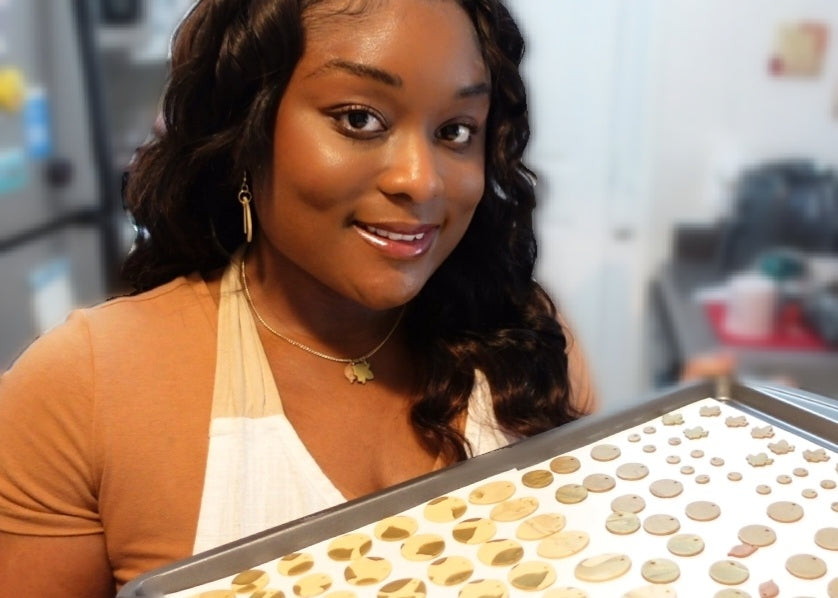 woman looks up and smiles while holding baking sheet of beige polymer clay earring pieces