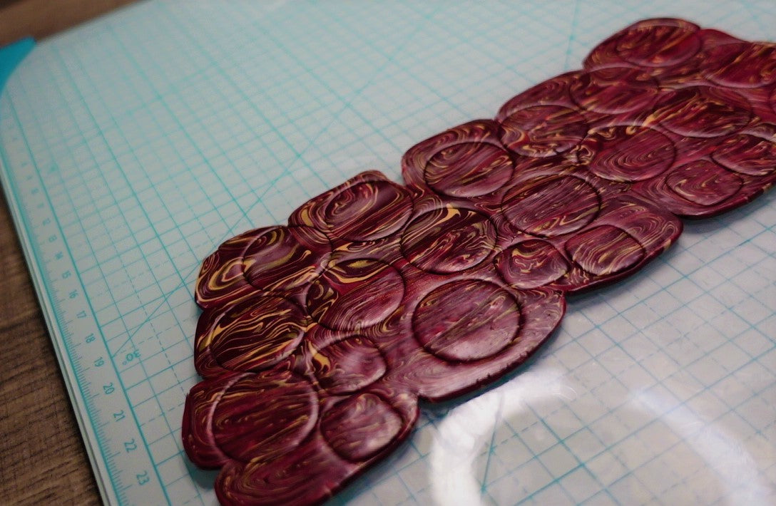 marbled burgundy and beige slab of polymer clay with circular cut-outs in varying sizes laying atop a light blue craft tile